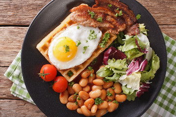 hearty breakfast with fried egg, waffles, bacon, mix salad and beans close-up. horizontal top view