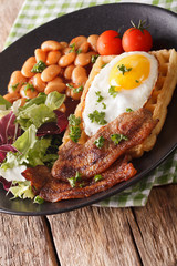 Delicious breakfast: fried egg, waffles, bacon, beans and salad close-up. vertical