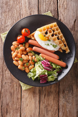 Savory breakfast: waffles with egg, sausages, beans and fresh salad close-up. Vertical top view