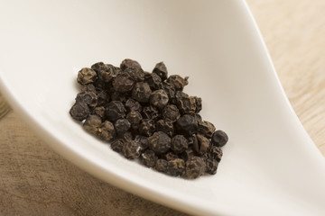 black pepper in white spoon on wooden background