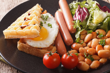 Delicious breakfast: fried egg, waffles, sausages, beans and salad close-up. horizontal