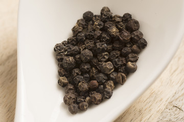 black pepper in white spoon on wooden background