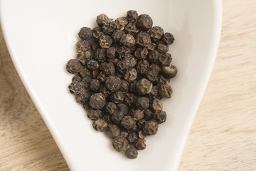 black pepper in white spoon on wooden background