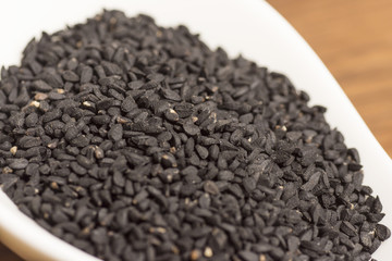 black seeds in white spoon on wooden background
