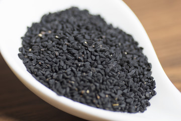 black seeds in white spoon on wooden background
