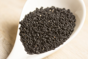 black seeds in white spoon on wooden background