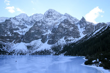 Panorama of frozen lake surrounded by mountains. People walk on the ice