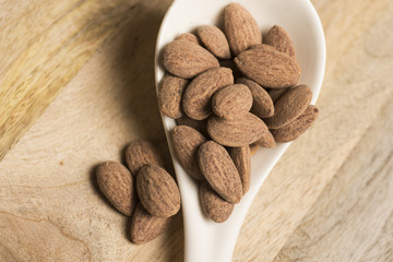 closeup of salt almonds nut in white spoon wooden background