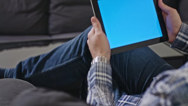 Poland, Lublin - 30 jan 2017: Man uses a digital tablet with a blue screen at home. In the background is neither black coffee table and sofa