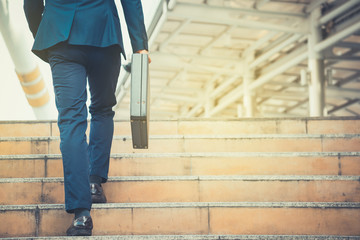 Business man holding a briefcase walking up the stairs in the routine of working with determination...