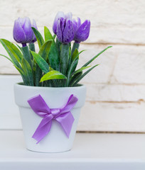 Decorative purple tulips in a white flower pot with a purple bow on the white stone background.