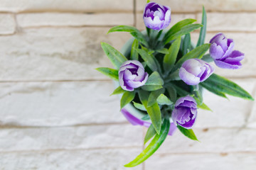 Decorative purple tulips in a white flower pot with a purple bow on the white stone background.