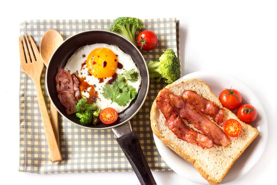 Breakfast with fried egg and bacon in dark pan on the table