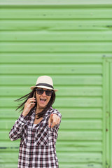 Happy beautiful woman talking on the phone over green background. Wearing hat and sunglasses.