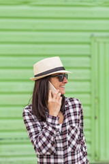 Happy beautiful woman talking on the phone over green background. Wearing hat and sunglasses.