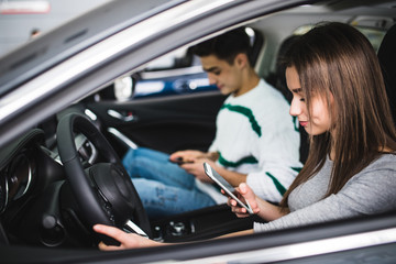 Portrait of a young couple use phones, texting and driving together, as seen through the windshield
