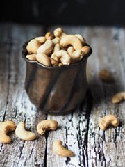 Copper cup full of cashew nuts on an old wooden background
