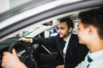 Fototapeta na wymiar Let me show you interior of this car. Handsome young classic car salesman standing in the dealership and helping a client to make a decision about new car