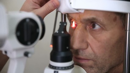 Dolly sliding towards male patient with head in medical device for examining eye structure.