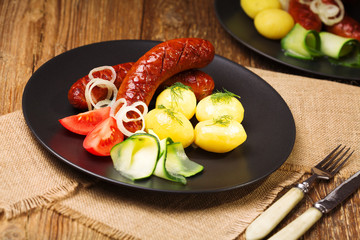 Grilled sausages in a pan with onions, served with boiled potatoes, zucchini and tomatoes.