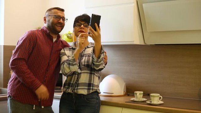 Couple making duckfaces while doing selfies on smartphone in the kitchen
