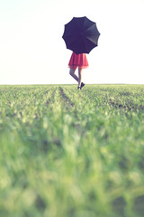 woman hides behind a black umbrella on a spring day on a green grass