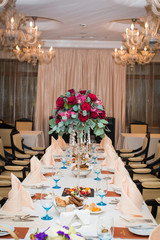 Wedding arrangement with fresh red roses, orchids and eucalyptus on the banquet table