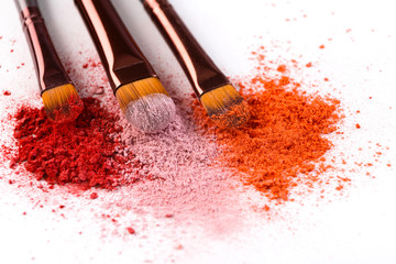 Makeup brushes with blush or eyeshadow of pink, red and coral tones sprinkled on white background