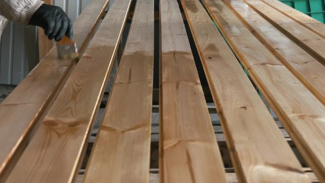 Impregnation and imbibition of vertically arranged wooden bars with a brush. Construction and painting works from wood. Varnishing and gloss of wood in the shop. Reflection of pine material.
