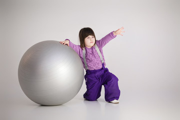 little girl in purple clothes with big ball for fitness on gray 