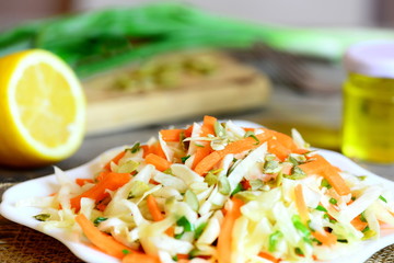 Simple coleslaw salad. Coleslaw salad with fresh carrots, green onion and pumpkin seeds on a plate. Salad ingredients on a wooden table. Healthy vegetable food. Closeup