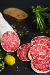Salami sausage sliced with rosemary, olives and spices on the dark background. Shallow depth of field.