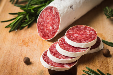 Salami sausage sliced with rosemary, olives and spices on the dark background. Shallow depth of field.