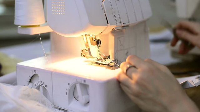 Seamstress quickly inserts a thread with tweezers white overlock. Dressmaker under the light bulb filament is passed through the hole and stretches it forward with the aid of a special metal clamp. On