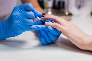 Professional beautician applying nail polish to female nail in a nail salon.