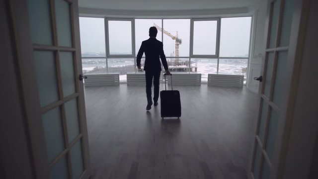 rear back view businessman enters the modern contemporary empty room with suitcase. Man celebrating success in new apartment.