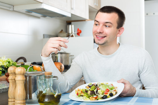 Man eating vegetable salad in kitchen.