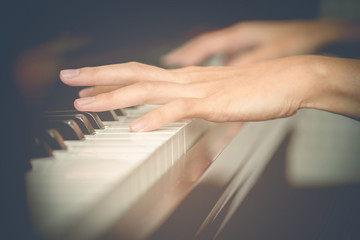 Close up of young girls hands, playing piano. vintage filter effect.