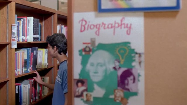Student choosing a library book from a high school library shelf