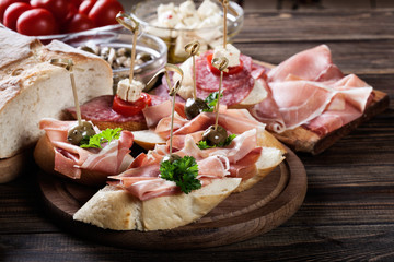 Spanish tapas with slices jamon serrano, salami, olives and cheese cubes on a wooden table