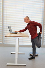 leg exercise during standing office work -  middle age balding man in eyeglasses man  with laptop at the mobile table