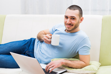 Young man using laptop and drinking coffee at his home.