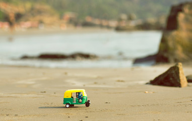 Tiny model of auto rickshaw moves across a sandy Goa beach in India.