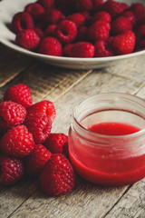 Raspberry syrup (jam) in a jar and berries raspberries on a wooden table