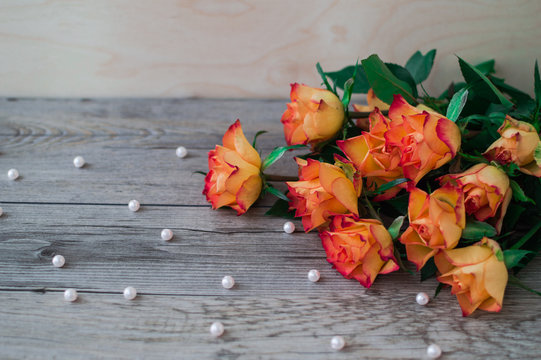 Bunch of beautiful orange rose on a light gray wooden background and scattered beads of pearls. The best gift on birthday and other holiday.