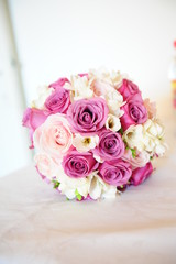 Wedding bouquet with different roses with pink hues positioned on a white cushion 