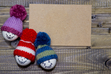 Easter eggs on wood. Emoticons in knitted hat with pom-poms. Handmade.