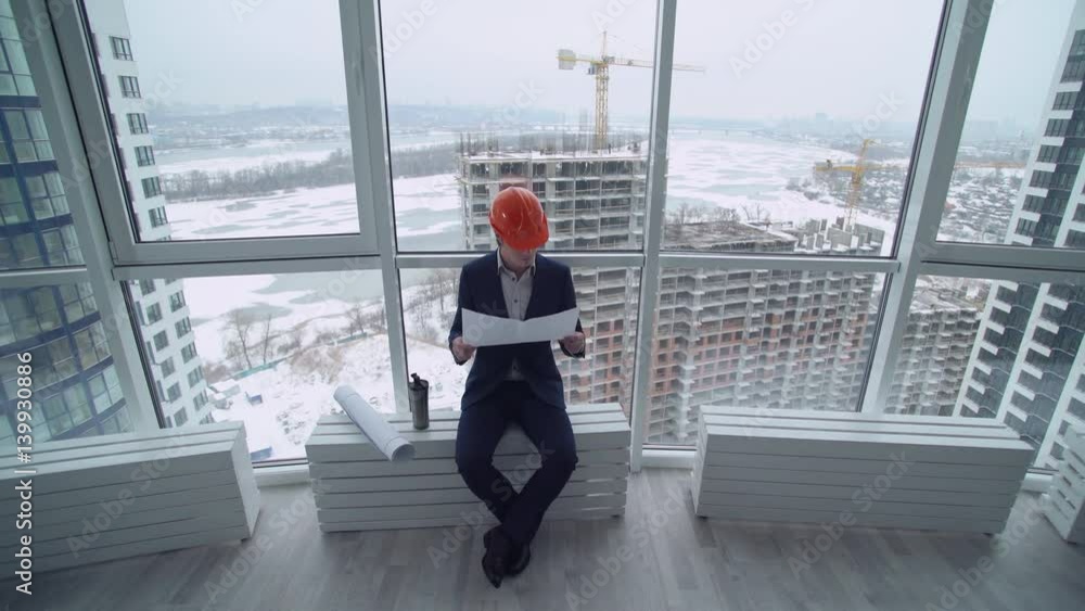 Aufkleber building engineer or architect have a break enjoy coffee holding documents. Handsome man wearing in elegant suit and orange hard hat. On the background construction site workers built house.
