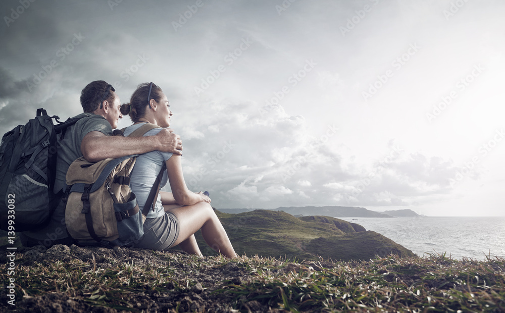 Wall mural Couple tourists with backpacks enjoying sunset on top of a mountain