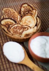 Cooked homemade pancakes on a dining table in a wicker plate next to sour cream for breakfast. Sweet dessert. Homemade cooking. With your own hands. Homemade